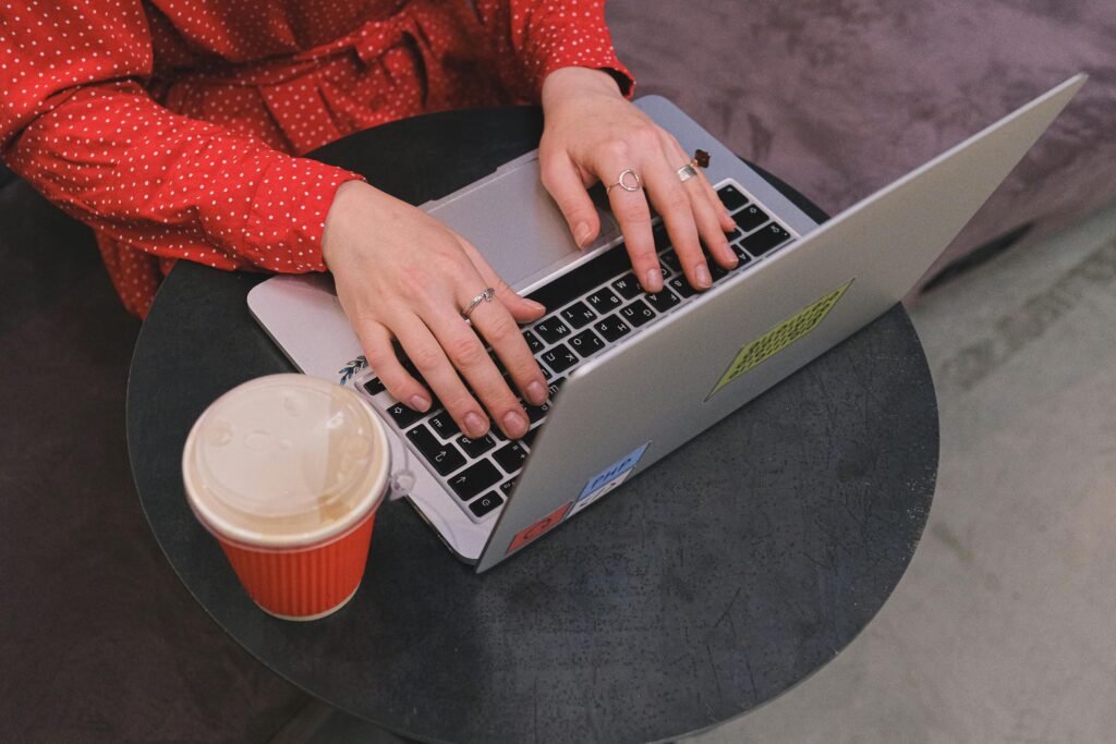 pexels-photo-12662880-12662880 A woman in a red polka dot dress typing on a laptop with coffee nearby.